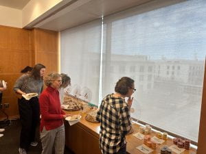 A group of people line up near a window to grab empanadas and sauce cups from trays positioned on top of a wooden ledge.